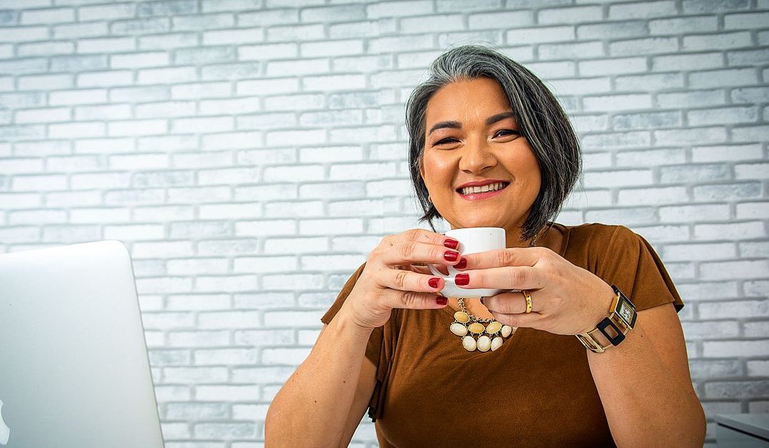 A smiling woman working on a laptop with a coffee, reviewing traffic, conversion and commission figures for a psychic affiliate website