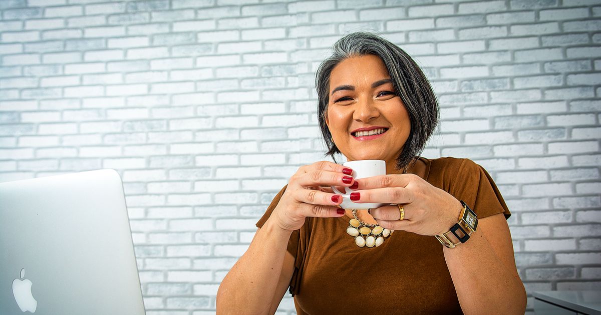 A smiling woman working on a laptop with a coffee, reviewing traffic, conversion and commission figures for a psychic affiliate website